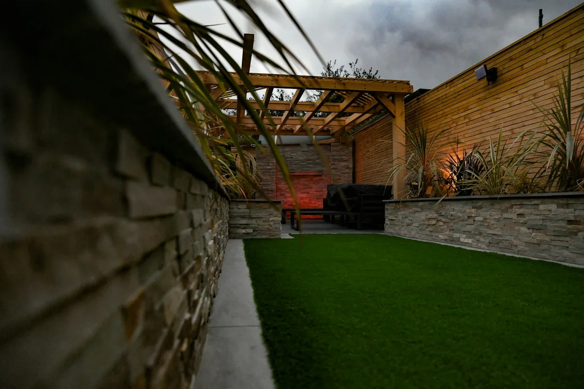 Stone-faced raised garden beds, timber screening and a lawn in a landscaped courtyard